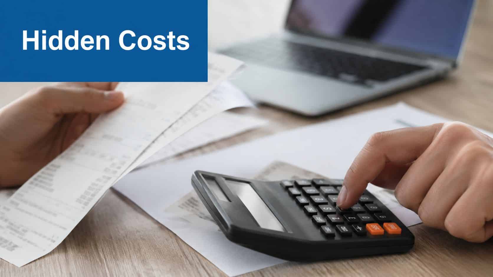 A person reviewing financial receipts while using a calculator and a laptop on a wooden desk.